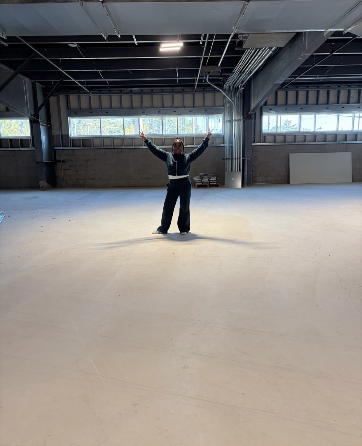 The empty studio space inside HUB 07, concrete floor and steel beams, one person standing at the center with both arms raised